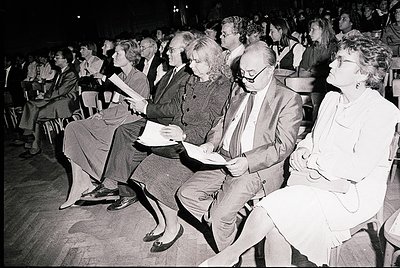 Black-and-white audience at a seated event, likely a lecture or performance, with attendees focused on the stage. Mid-20th ce...