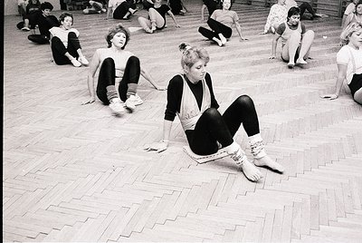 Group of women in mid-20th-century dance practice, likely 1960s–1970s, on polished wooden floor. Casual attire—leggings, swea...