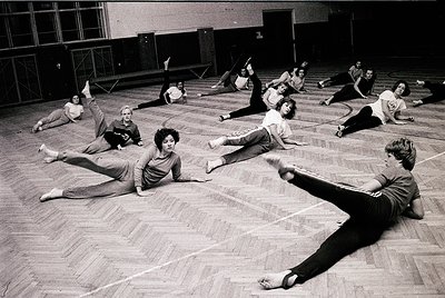 Black-and-white gym class in mid-20th century (likely 1960s–70s) with students performing floor exercises in a spacious indoo...