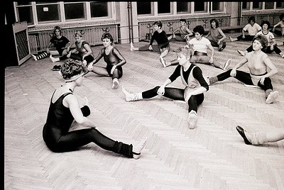 Black-and-white gym class featuring young students in leotards and tights performing floor exercises, 1960s–1970s. Wooden flo...