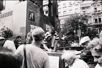 A candid 1970s street scene in a European city, likely . A group of people gathers around a makeshift barricade, with one man...