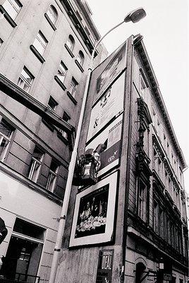 Mid-century urban facade featuring vintage billboards on a multi-story building. Prominent ads include a 1960s-era perfume ca...