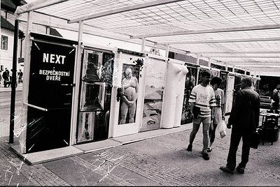 Vintage outdoor photo exhibit under a tented structure, featuring black-and-white portraits and landscapes. Signage in Czech ...