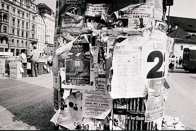 A dense cluster of vintage posters and flyers covers a lamppost in an urban setting, featuring election campaign materials (,...