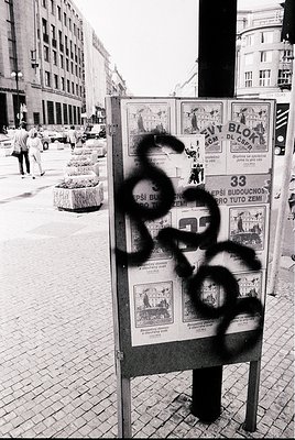 Vintage urban poster board in Eastern Bloc-style city, featuring graffiti "68" over a 1968 housing campaign ad. Buildings exh...