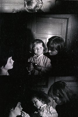 Vintage black-and-white photo of a family moment: a woman holding a child in a doorway, another child peering over her should...