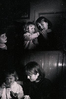 Vintage black-and-white split photo of three children in a dimly lit room, likely mid-20th century. Top: Two children hugging...