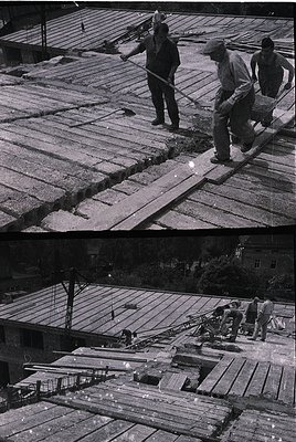 Mid-20th century construction crew installing wooden planking on a rooftop, likely for a flat or sloped roofing system. Worke...