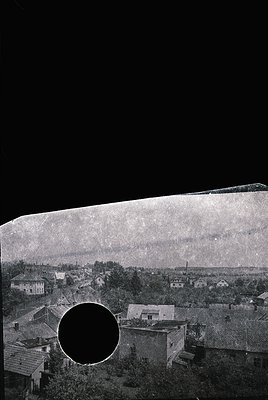 Vintage viewfinder photograph showing a rural settlement with low-slung brick houses and dense greenery. Circular aperture re...