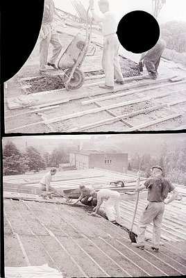 Vintage black-and-white construction site featuring manual laborers laying wooden planks on a foundation. Workers in rolled-u...
