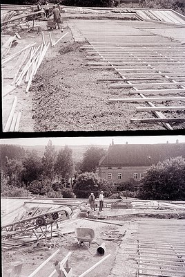 Mid-20th century construction site featuring wooden framing and concrete work. Two workers in mid-century attire (one in top ...