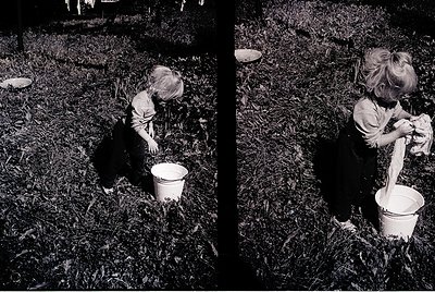 Two children in mid-20th-century rural attire dig in a grassy field, each holding a white bucket. Clothing suggests 1950s–196...
