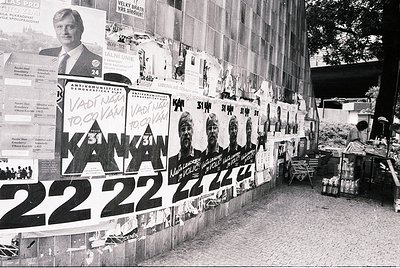 Wall covered in anti-communist campaign posters, featuring prominent figures and slogans like "KAN KAN" and "22.22" alongside...