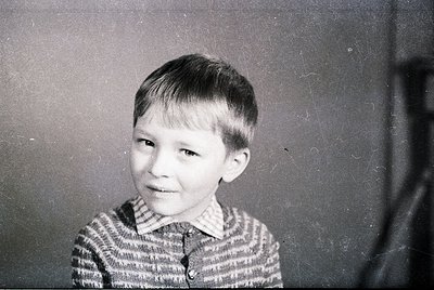 Vintage black-and-white portrait of a young boy with short, neatly parted hair, wearing a striped sweater. Indoor setting wit...