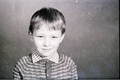 Black-and-white portrait of a young boy in a striped sweater, likely mid-20th century. Plain backdrop suggests school or stud...