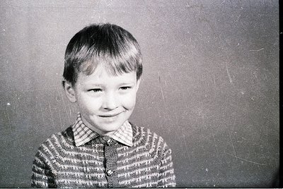 Vintage black-and-white portrait of a young boy in a striped sweater, mid-20th century style. Plain backdrop suggests studio ...