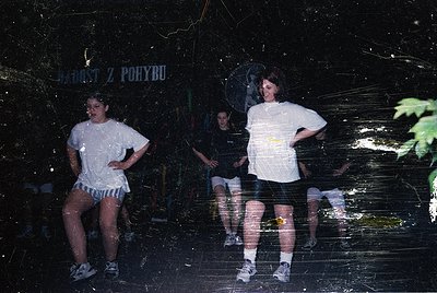 Vintage photo of three individuals posing against a dark, textured wall with Czech signage ("JÁROST Z POBYTU"). Casual 1980s–...