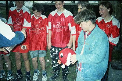 Young soccer team from **ZS Libeznice** (Czech Republic) in 1980s–90s jerseys, posing with coach. Wet grass and muddy field i...