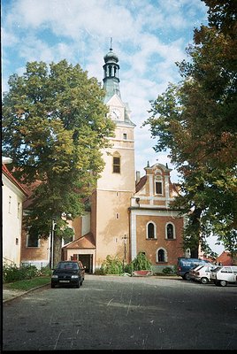 Historic church with Baroque-style tower and clock, featuring cream brickwork and arched windows. Surrounded by mature trees ...