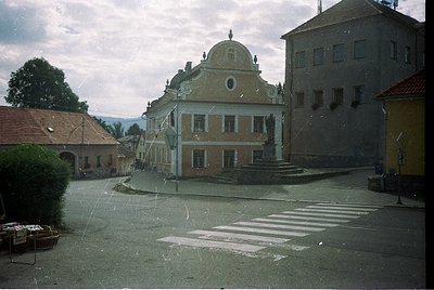 Neoclassical building with domed roof and decorative facade in a European village square, likely 1970s–1980s. Crosswalk and v...
