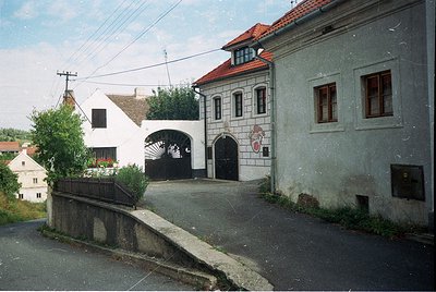 Eastern European village street with mid-20th century architecture—gray stucco buildings featuring arched entryways, wooden s...