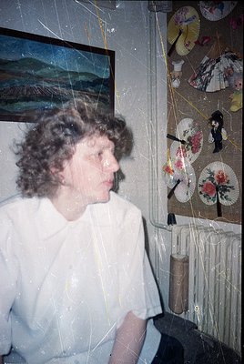 Vintage portrait of a woman in a white blouse, blurred for privacy, standing beside a wall adorned with decorative paper fans...