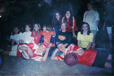 Vintage group photo of a youth basketball team in a dimly lit gym, likely from the **1970s–1980s**. Players in red/white stri...