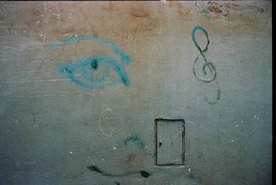 Graffiti of a stylized eye and treble clef symbol on aged, weathered concrete wall. Minimalist design with faded turquoise pa...
