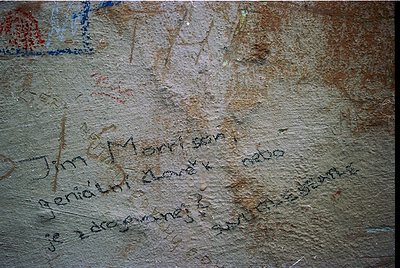 Graffiti etched into weathered stone wall, featuring faded inscriptions in Cyrillic script. Visible text includes "Jim Morris...