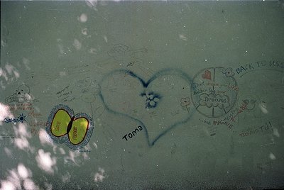 Vintage graffiti-covered glass window with etched messages, including a large heart and circular designs. Visible inscription...