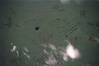 A close-up of a concrete surface covered in graffiti from the 1970s–1980s, featuring peace symbols, handprints, and messages ...