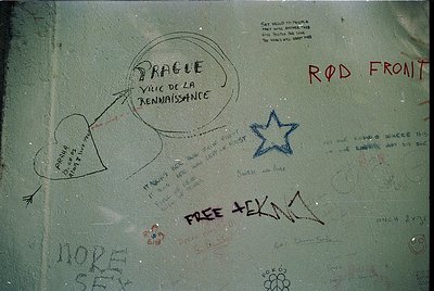 Graffiti-covered metal surface with handwritten messages in various styles, including "Prague Ville de la Renaissance," "Rod ...