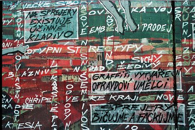 Vibrant graffiti wall featuring bold, layered text in Czech/Slovak with red, white, and black paint. Prominent phrases includ...