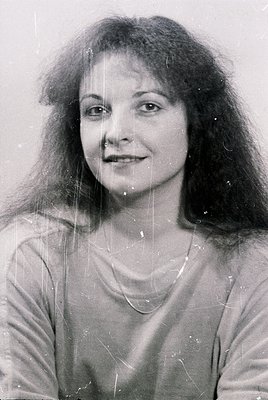 Portrait of a woman with voluminous, shoulder-length curly hair, shot in black-and-white. She wears a simple necklace and a l...