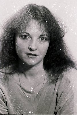 Black-and-white portrait of a woman with voluminous shoulder-length hair, shot in mid-20th century style. Her direct gaze and...