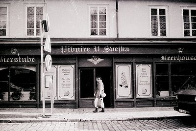 Black-and-white shot of a historic European beer hall, *Pivnice U Svíčka*, featuring ornate signage in Czech. The building’s ...