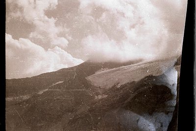 Vintage sepia-toned aerial view of a snow-covered mountainous landscape with a winding road cutting through terrain. Evidence...