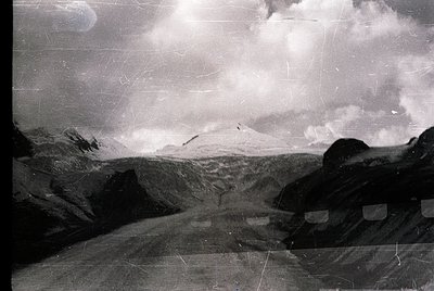 Vintage black-and-white alpine landscape with rugged peaks and dramatic cloud formations. Foreground shows weathered stone st...