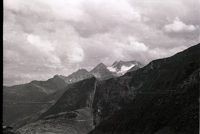 Vintage black-and-white alpine landscape featuring jagged peaks and steep slopes under dramatic cloud cover. Evidence of earl...