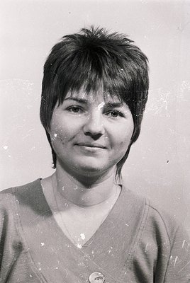 Portrait of a woman with short, angled bangs and a neutral expression, likely taken in the 1970s–1980s. She wears a simple V-...