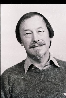 Black-and-white portrait of a man with a mustache and beard, wearing a collared sweater. Mid-century styling suggests 1960s–1...