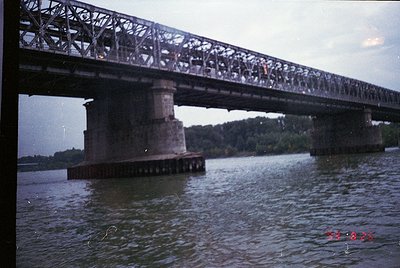 Vintage steel truss bridge spanning a river, supported by concrete piers. Crowds of people walking across, suggesting mid-20t...