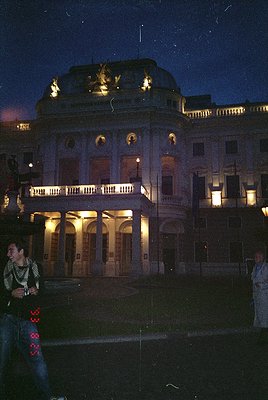 Neoclassical building illuminated at dusk, featuring symmetrical arches, columns, and a central pediment with sculptural reli...