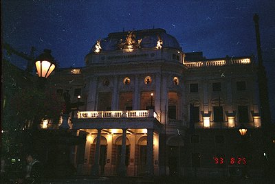 Neoclassical building illuminated at dusk, featuring symmetrical columns, arched windows, and decorative balustrades. The cen...