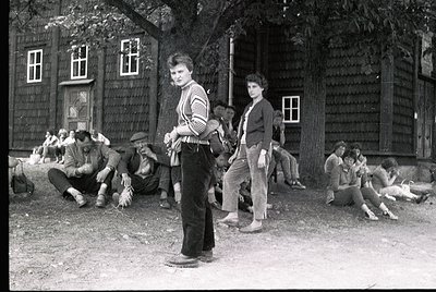 Black-and-white snapshot of a rural gathering, likely Eastern Europe, 1960s–1970s. Group of young people in casual attire—str...