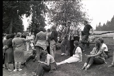 Vintage outdoor gathering of young adults in 1960s-70s attire, likely a youth camp or social event. Group of ~20 people in ca...