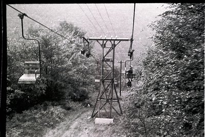 Mid-20th century ski lift with vintage metal chairs suspended on cables, surrounded by dense forest. Snow-covered terrain and...