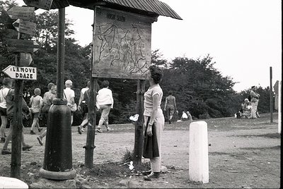 Black-and-white photo of a rural roadside scene with a wooden signpost displaying Cyrillic text ("НАРОДНА СЛОБОДА") and a car...