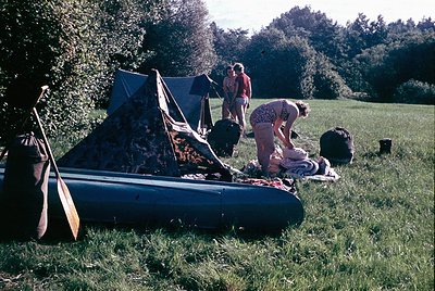 Vintage outdoor camping scene with inflatable raft and vintage tent. Two adults (one in floral dress, one in striped shirt) s...
