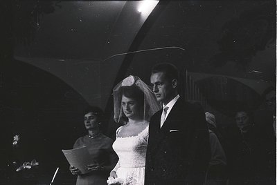 Mid-20th century black-and-white wedding portrait: bride in classic veiled gown, groom in dark suit, holding hands under dram...
